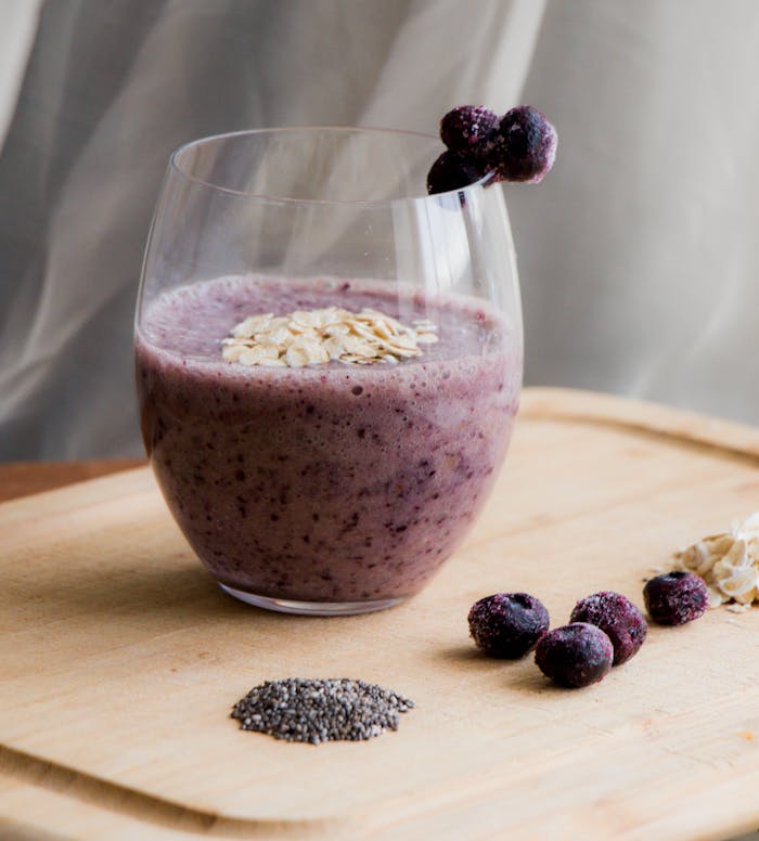 Delicious blueberry smoothie with chia seeds and oats in a clear glass on wooden surface.