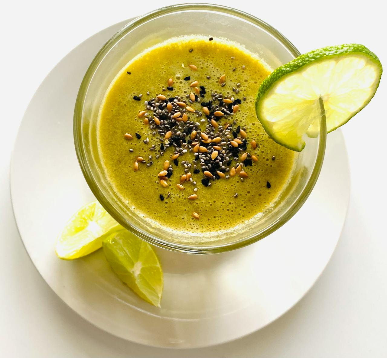 Overhead view of a green smoothie with sesame seeds and lime on a saucer.