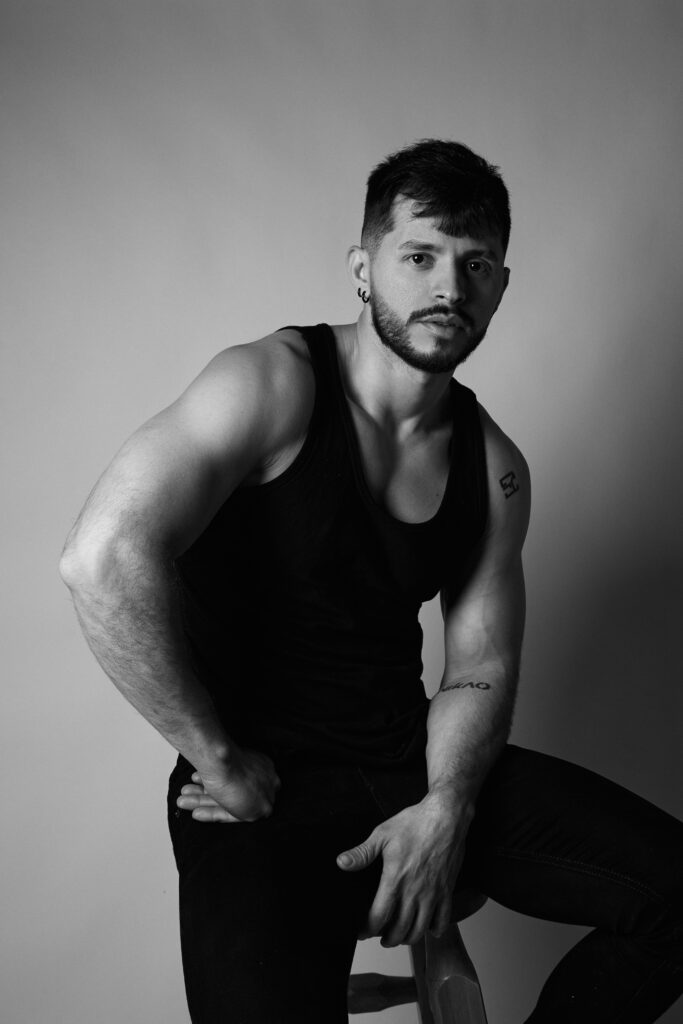 Monochrome image of a fit man sitting confidently in a studio setting.